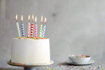 White birthday cake with colorful striped candles and sprinkles.